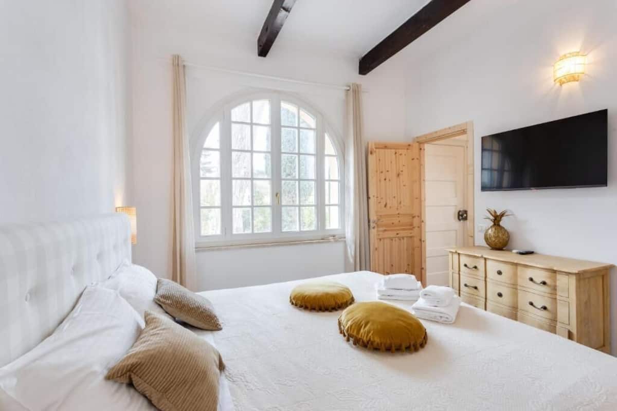 A bedroom with a large bed, a wooden wardrobe, a flat-screen TV, and a window with curtains.