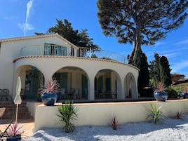 Una villa de estilo mediterráneo con un porche cubierto, mobiliario exterior y plantas en macetas.
