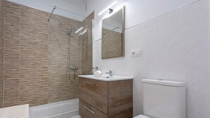 Un baño moderno con tocador de madera, lavabo blanco, espejo y zona de ducha.
