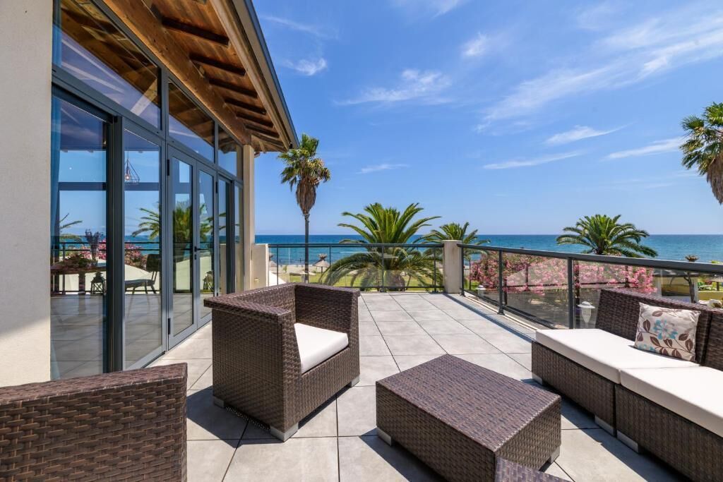 A balcony with wicker furniture, glass doors, and a view of the sea.