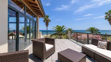 A balcony with wicker furniture, glass doors, and a view of the sea.