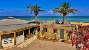A beachfront restaurant with a patio area, palm trees, and a view of the sea. - Hotel San Pellegrino (Penta-di-Casinca)