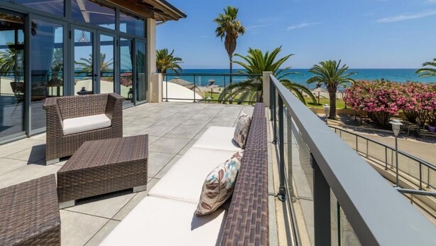 A balcony with wicker furniture, a glass door, and a view of the sea. - Hotel San Pellegrino (Penta-di-Casinca)