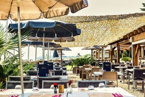 Een buitenterras met meerdere tafels en stoelen, afgedekt met parasols, en een decoratief plafond.