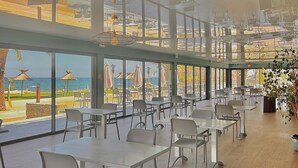 A spacious dining area with large windows, modern furniture, and a view of the beach. - Hotel San Pellegrino (Penta-di-Casinca)