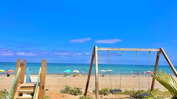 A beach with a wooden swing set and a staircase leading to a shaded area.