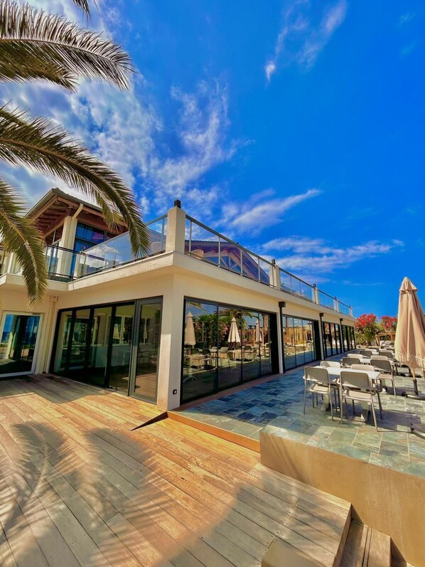 A modern outdoor patio area with a pool, glass-enclosed dining area, and a covered seating area with umbrellas.