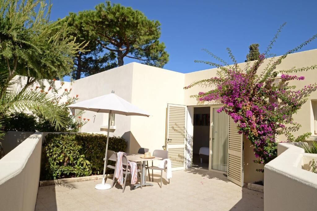 A patio with a table and chairs, a white umbrella, and a door leading to a room.