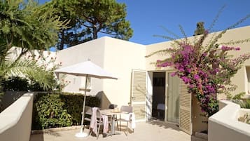 A patio with a table and chairs, a white umbrella, and a door leading to a room.
