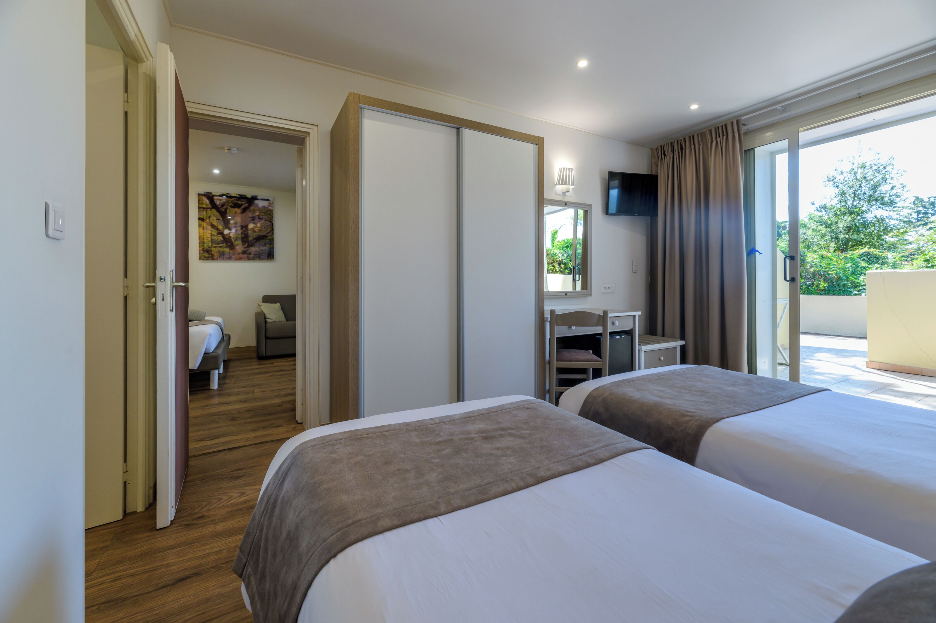 Une chambre d’hôtel avec deux lits, un bureau, une chaise et une porte coulissante donnant sur un balcon.