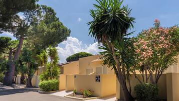 A residential area with a yellow building, a parking lot, and various trees and shrubs.