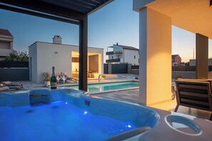 A modern outdoor pool area with a hot tub, lounge chairs, and a view of neighboring buildings. - Private & Modern 4BR Villa, Heated Pool, Jacuzzi, and Gaming room, Near Zadar (Bibinje)