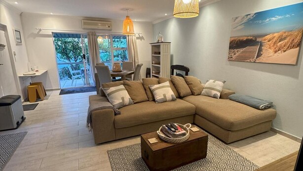 A living room with a sectional sofa, a coffee table, and a large window with a view of the outdoors. - Tranquil Cottage Retreat - Malanshof, Randburg (Johannesburg)