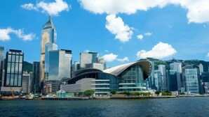 A modern city skyline with high-rise buildings and a distinctive curved structure near a body of water. - Leisure Hostel (Hong Kong)