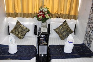 Habitación de hotel con dos camas, cada una con un cojín, una mesita de noche con teléfono y un jarrón de flores.