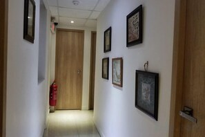 A hallway with framed pictures on the walls, a wooden door at the end, and a red fire extinguisher on the left. - Leisure Hostel (Hong Kong)