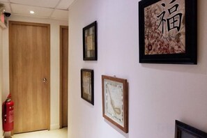 A hallway with framed artwork on the wall, a wooden door, and a fire extinguisher. - Leisure Hostel (Hong Kong)