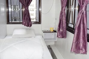 Una habitación de hotel con cama, mesita de noche, lámpara y ventana con cortinas.