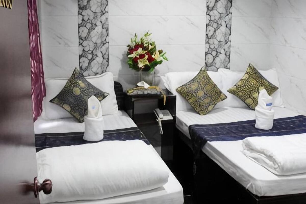 A hotel room with two beds, each with a pillow, a bedside table, a vase with flowers, and a towel on the bed.