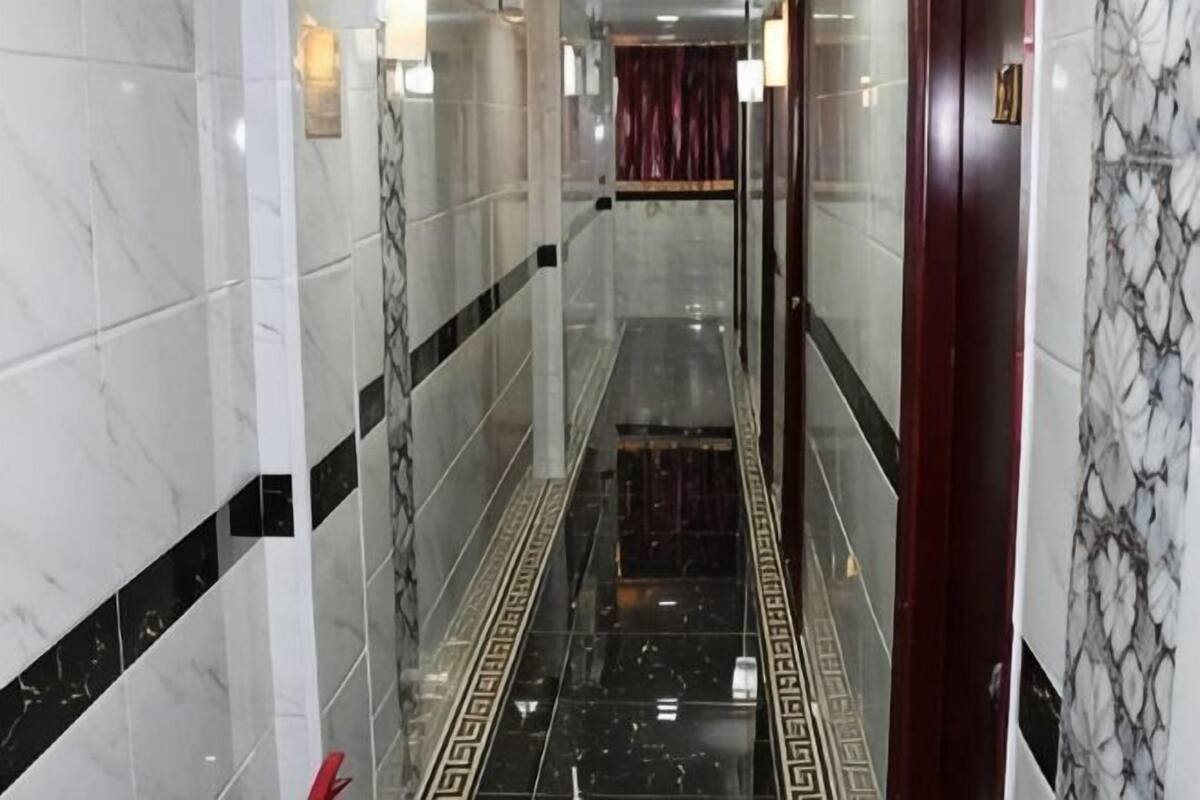 A corridor with marble walls and a patterned floor, leading to a room with a red curtain.