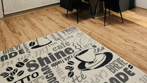 Zona pranzo con tavolo e due sedie, un termosifone, una finestra con tende e un quadro appeso al muro raffigurante cibo.