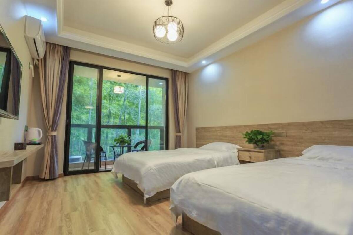 Une chambre d’hôtel avec deux lits, un bureau, une chaise et une grande fenêtre donnant sur un paysage verdoyant.