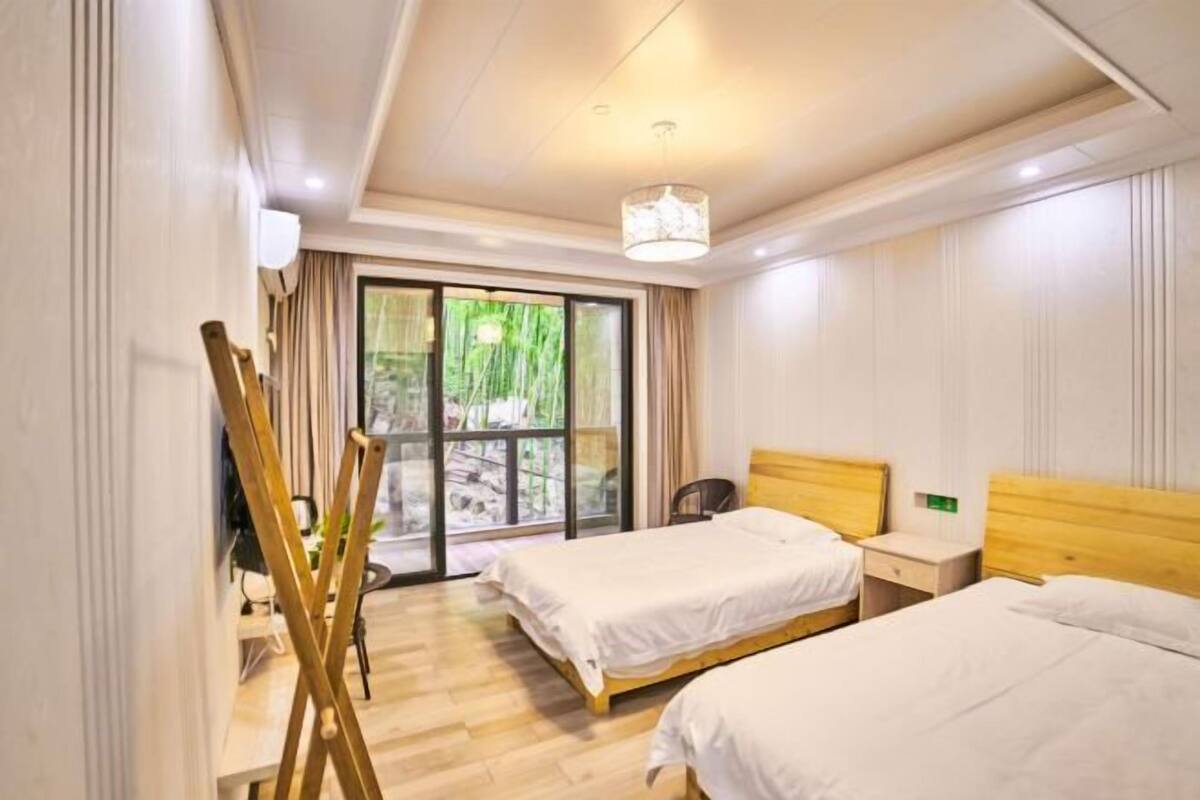 Une chambre d’hôtel avec deux lits, une tête de lit en bois, une grande fenêtre donnant sur un beau paysage et un luminaire au plafond.