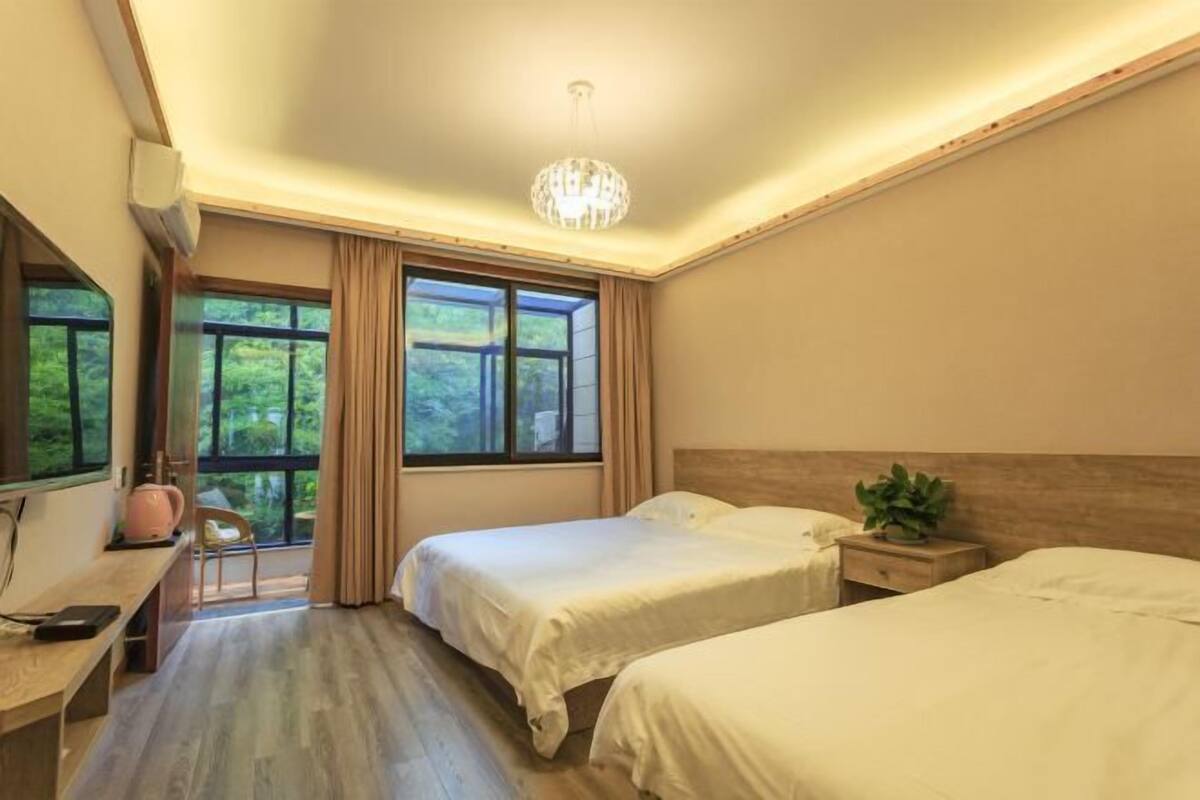 Une chambre avec deux lits, un bureau, une chaise, une fenêtre avec des rideaux et un lustre.