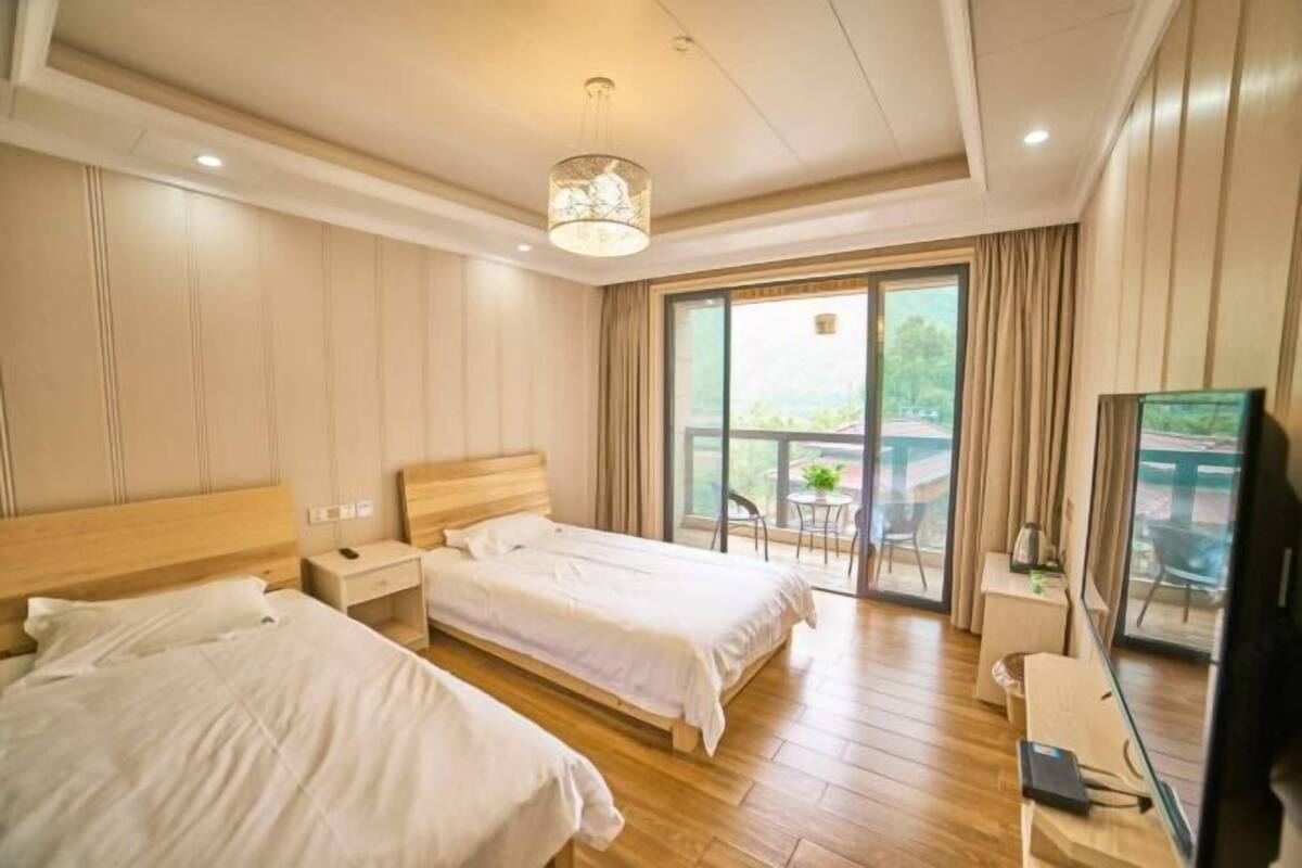 Une chambre d’hôtel avec deux lits, un bureau, une chaise, une télévision et un balcon avec vue.