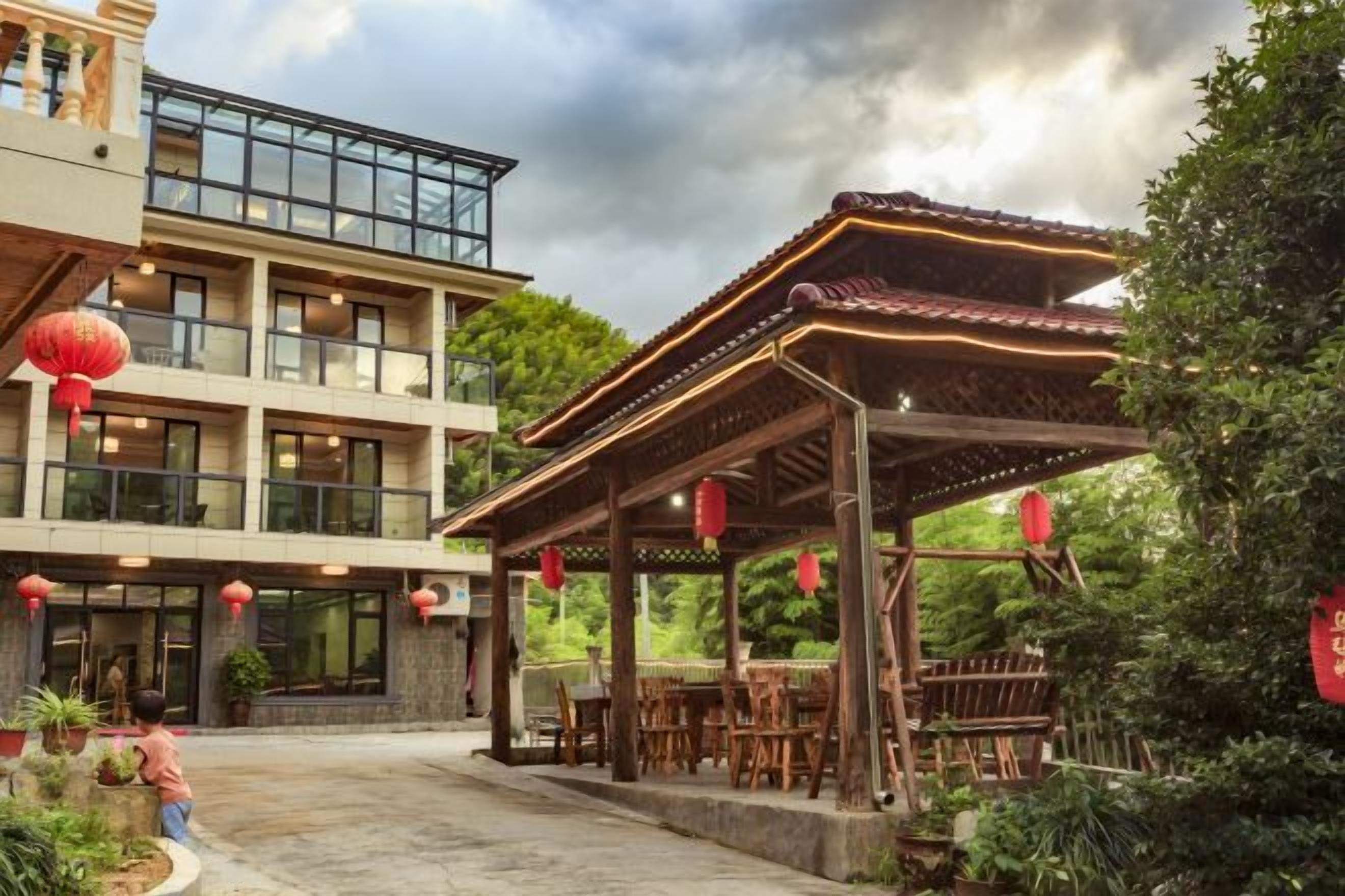 A traditional-style building with a covered outdoor seating area, surrounded by greenery and red lanterns.