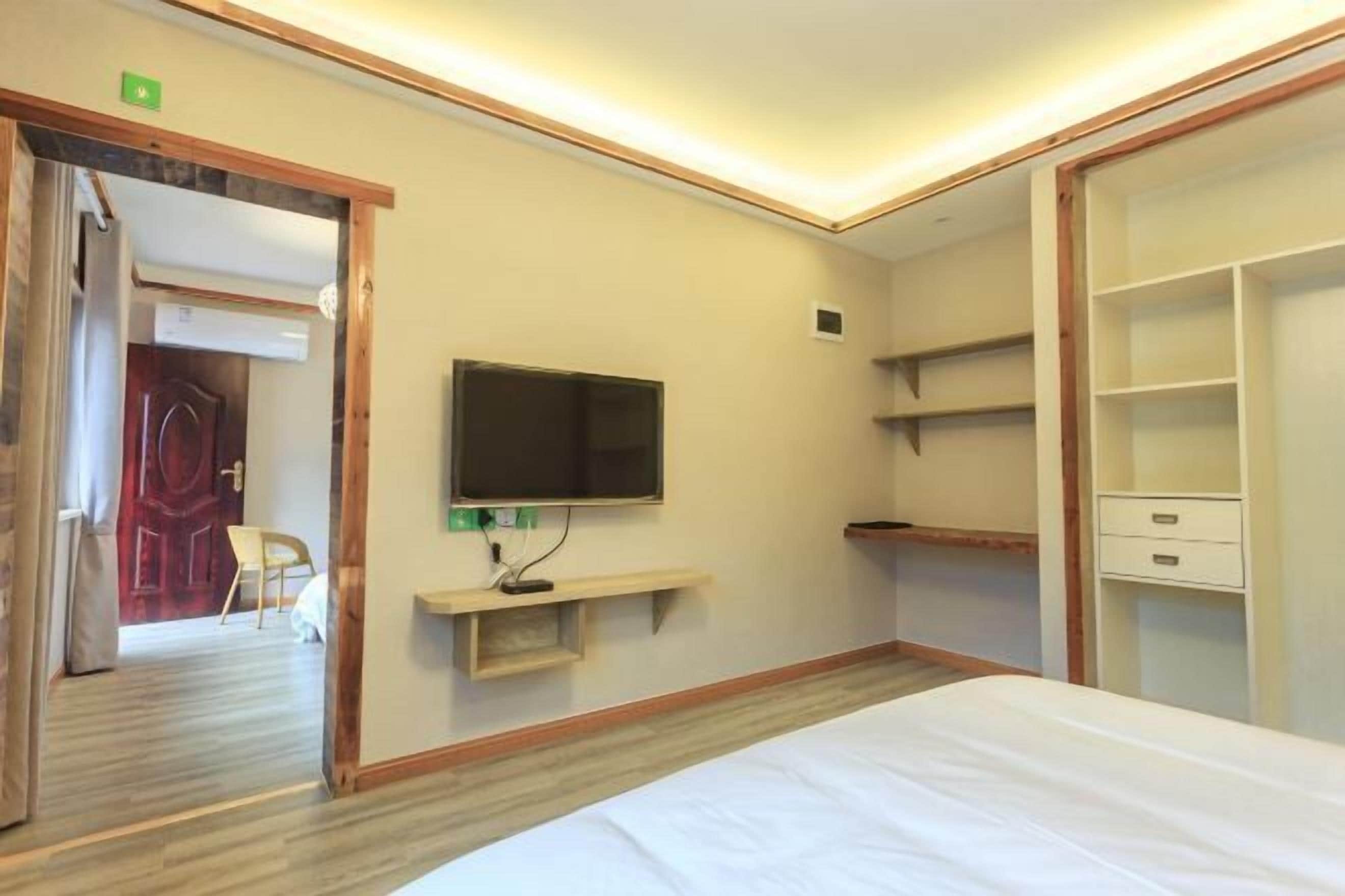 Camera d'albergo con un letto, una TV a muro, pavimento in legno e un armadio con ripiani.