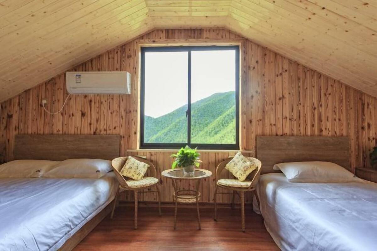 Une chambre avec deux lits, une fenêtre donnant sur la montagne, une petite table avec des chaises et un appareil de climatisation.