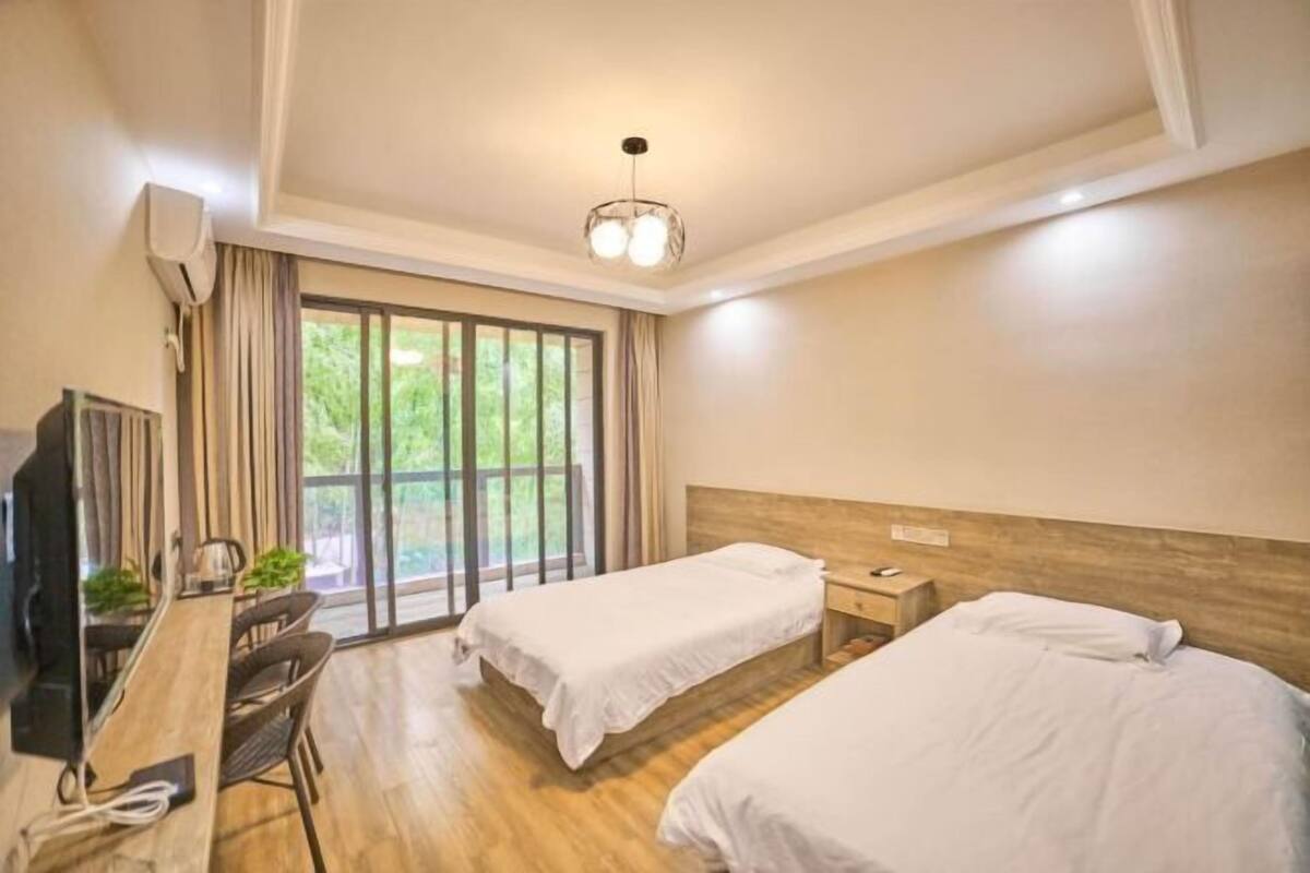 Une chambre d’hôtel avec deux lits simples, un bureau avec une chaise, une télévision et une grande fenêtre avec des rideaux.