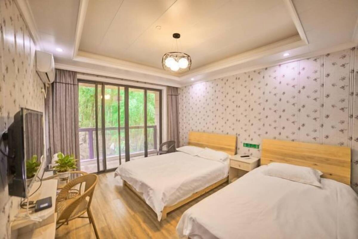 Une chambre d’hôtel avec deux lits, un bureau, une chaise, une télévision et une fenêtre donnant sur un paysage verdoyant.