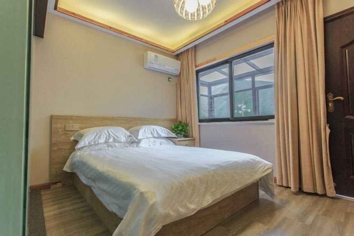 Une chambre à coucher avec un lit, une fenêtre avec des rideaux, un appareil de climatisation et une porte.