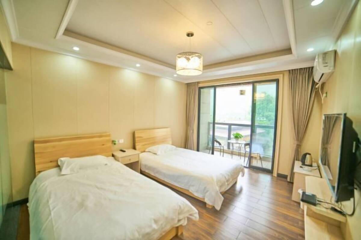 Une chambre d’hôtel avec deux lits, une télévision, un bureau et un balcon équipé d’une table et de chaises.