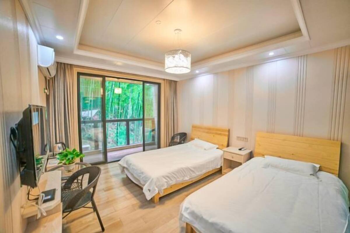 Une chambre d’hôtel avec deux lits, un bureau avec une chaise, une télévision et une grande fenêtre donnant sur un paysage verdoyant.