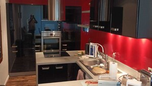 A modern kitchen with red and black cabinetry, stainless steel appliances, and a central island with a bowl of orange substance. - Lavandou Maison de Ville Duplex ,400 Mètres des Plages. Ideal Pour les Familles (Le Lavandou)