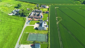 Oversigtsbillede af et landligt område med marker, en lille bebyggelse og en tennisbane.