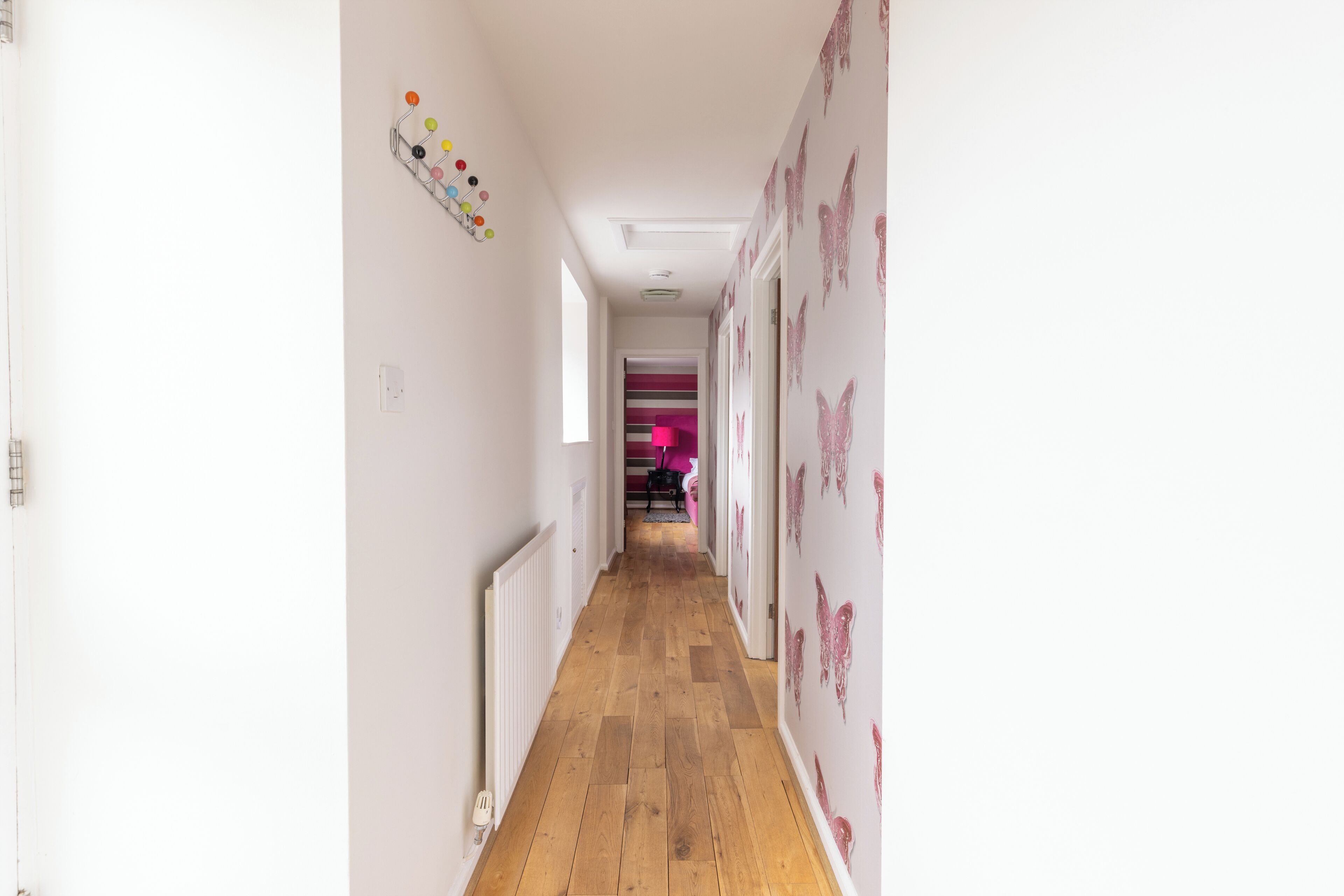 Un estrecho pasillo con suelo de madera, paredes blancas y adhesivos decorativos de mariposas.