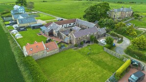 En stor ejendom med flere bygninger, heriblandt en hovedbygning med en stenfassade, forskellige udhuse og en velplejet græsplæne.