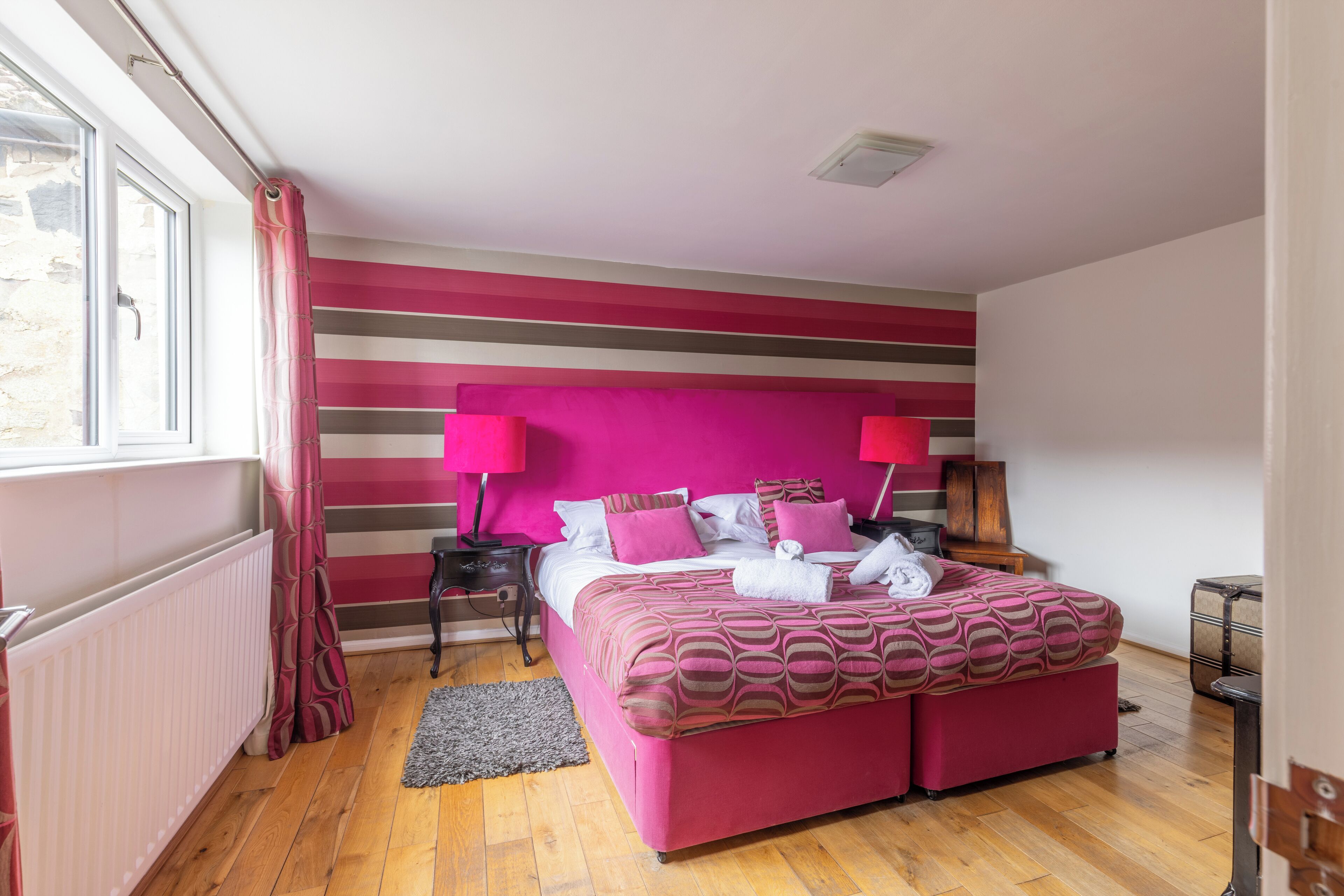 A bedroom with a large bed, striped walls, and a window with curtains.