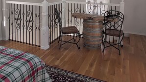 A room with a wooden floor, a bed with a plaid bedspread, a small table with a candle, two chairs, and a window with blinds. - Massage Chair, Tempurpedic Mattress, Amenity Claw Machine, 2 Story Loft House (Long Eddy)