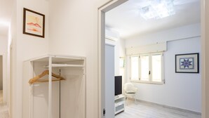 Une chambre dotée d’un dressing, d’une télévision, d’un fauteuil et d’une fenêtre avec des stores.