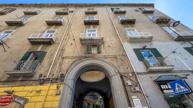 Un immeuble à plusieurs étages doté de balcons, d’une arche centrale et d’un panneau indiquant un passage piéton.