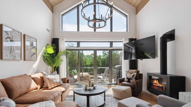 A spacious living room with a high ceiling, a fireplace, and a large window overlooking a deck. - Tremblant Prestige - Verbier 11-204 (Mont-Tremblant)