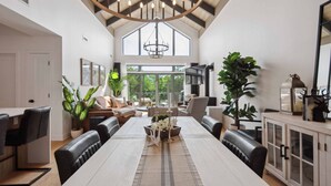 A spacious dining area with a high ceiling and large windows, featuring a long table, modern chairs, and a chandelier. - Tremblant Prestige - Verbier 11-204 (Mont-Tremblant)