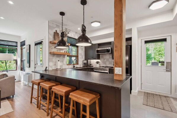 A modern kitchen with a large island, bar stools, pendant lighting, and a view of the outdoors.