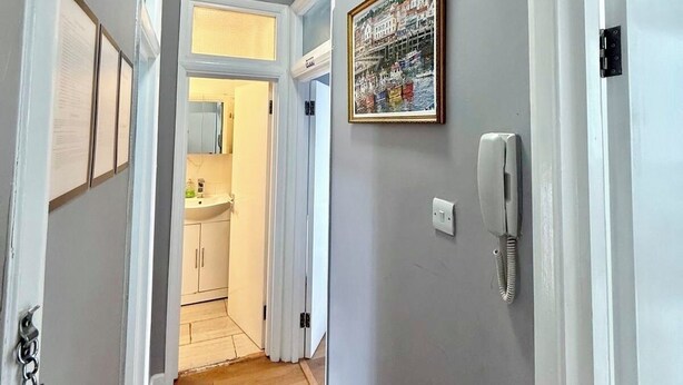 Ein Flur mit Holzboden, einer weißen Tür, einem fest installierten Telefon und einem gerahmten Bild.