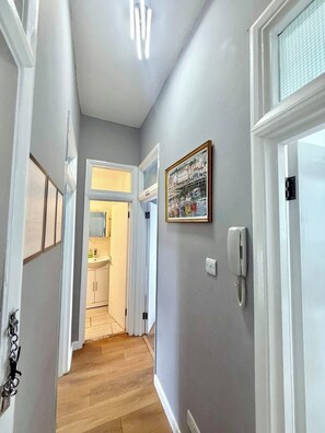 A hallway with a wooden floor, a white door, a wall-mounted phone, and a framed picture.
